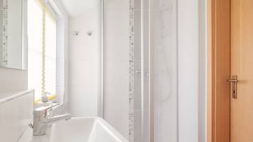 A modern bathroom with a white sink, a glass shower enclosure, and a wooden door.