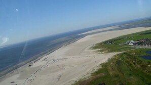 An aerial view of a coastal area with a sandy beach, a small settlement with buildings, and a body of water. - FEWO auf dem Lande (Tumlauer Koog)