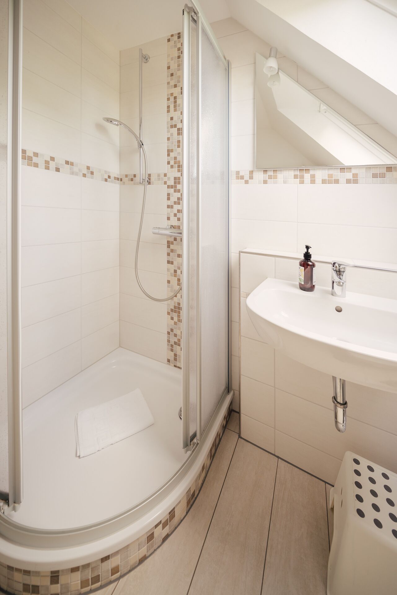 Ein modernes Badezimmer mit einer Glaskabine zur Dusche, einem weißen Waschbecken und einer gefliesten Rückwand.