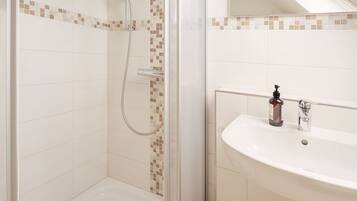 Ein modernes Badezimmer mit einer Glaskabine zur Dusche, einem weißen Waschbecken und einer gefliesten Rückwand.