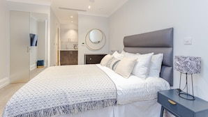 A modern bedroom with a large bed, a bedside table, a mirror, and a wardrobe.