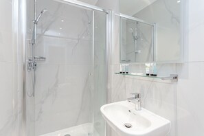 A modern bathroom with a glass-enclosed shower, a white sink, and a mirror above it. - Alexander Apartments (London)
