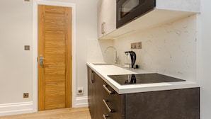 A modern kitchen with a wooden door, a built-in oven, a stainless steel kettle, and a marble backsplash.