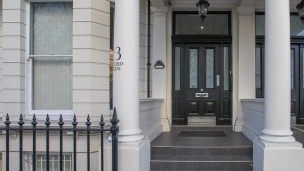 A building entrance with a black door, white columns, and a black iron fence.