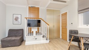A compact living space with a staircase, a sofa, a dining table, and a TV.