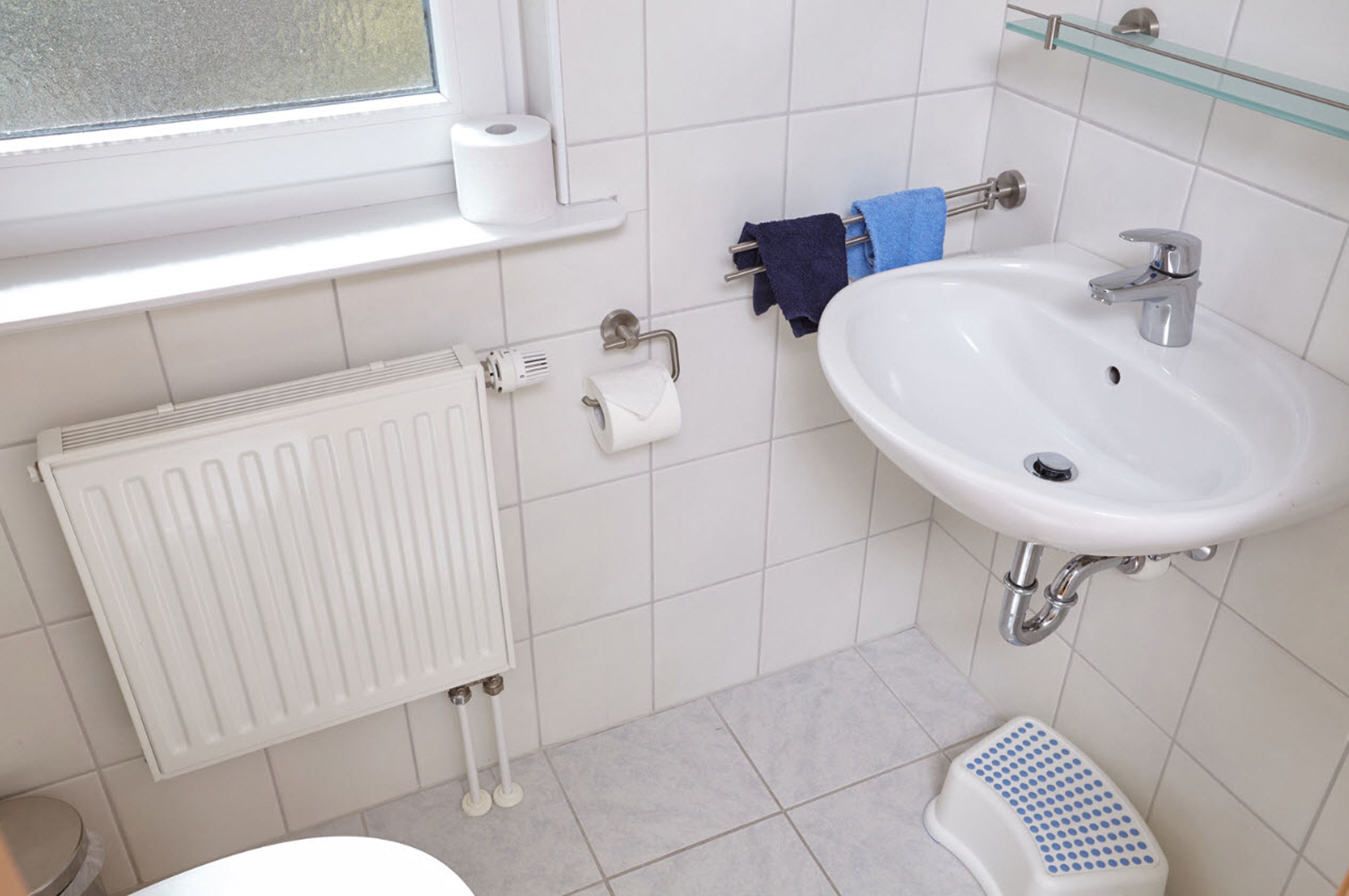 Un baño con un lavabo blanco, un espejo, toallero, inodoro y radiador.