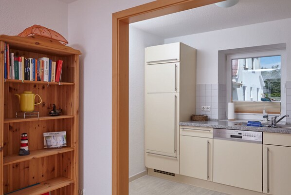 Una cocina con una estantería de madera, un refrigerador, un lavavajillas y un ventanal con vistas a edificios.