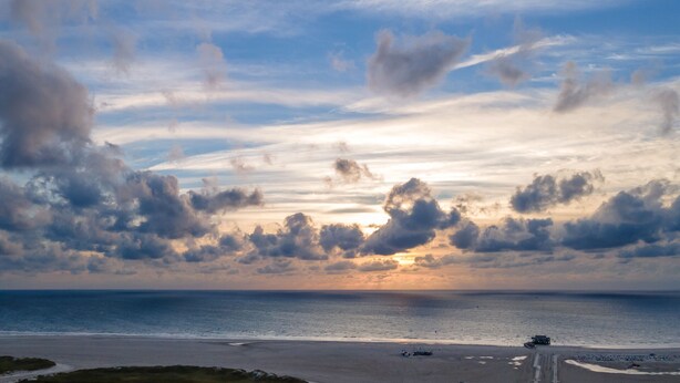 Una playa con un atardecer, nubes y cielo despejado.