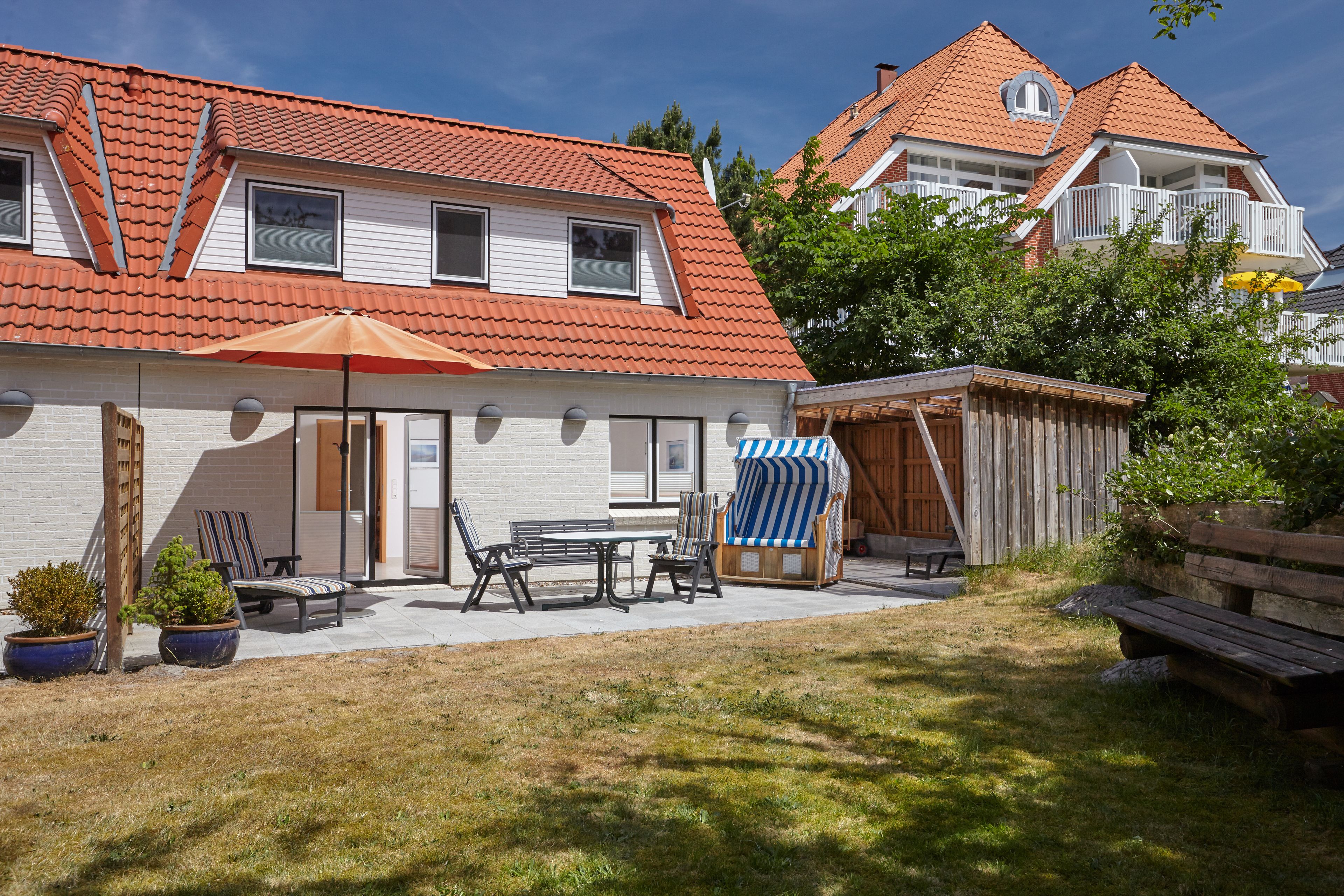 Een tweelaags huis met een dak van rode tegels, een terras met tuinmeubilair en een houten omheining.