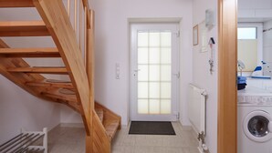 Un cuarto de lavado con lavadora, un radiador y una escalera de madera que conduce a otra habitación.