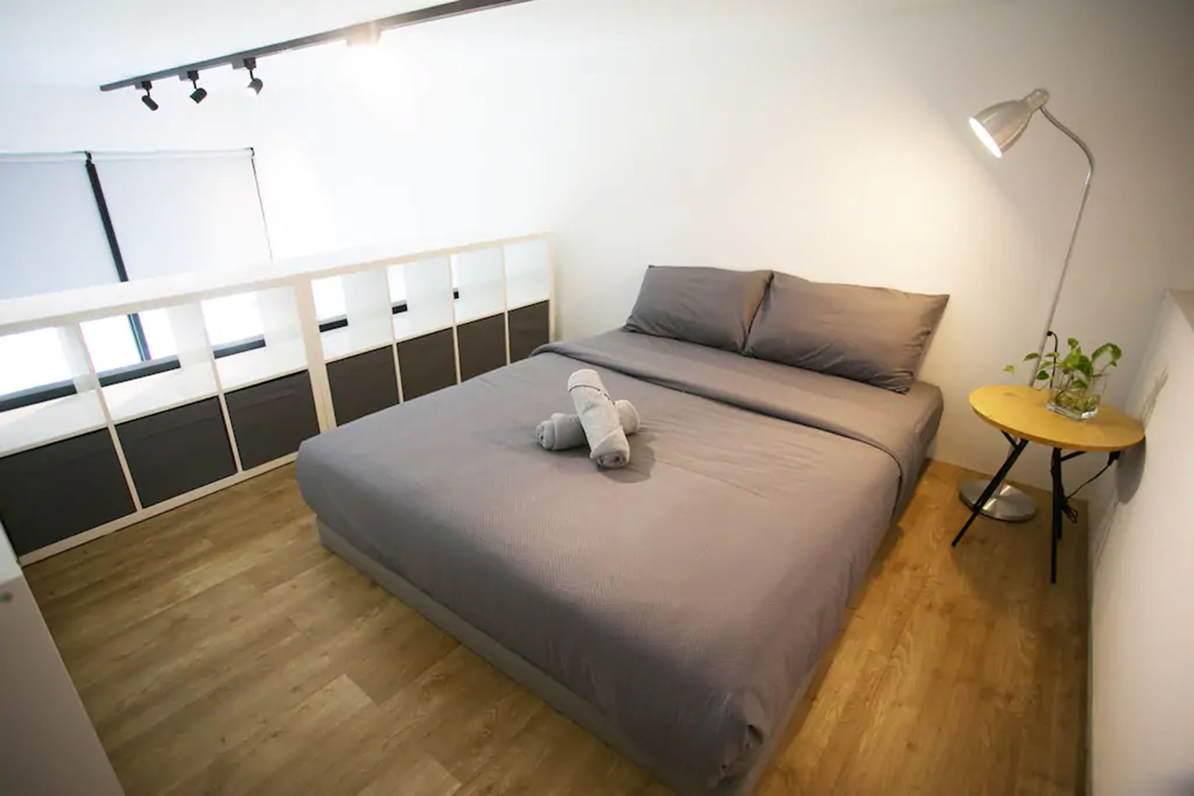 A bedroom with a bed, a bedside table with a lamp, and a small table with a plant.
