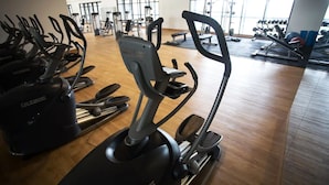 Ein Fitnessraum mit verschiedenen Trainingsgeräten, darunter Laufbänder und Crosstrainer, auf Holzboden.