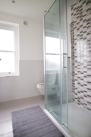 A modern bathroom with a glass shower enclosure, a toilet, and a window providing natural light. - Bedroom Flat in Heart of London (London)