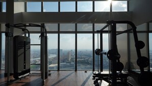 A gym with large windows, exercise equipment, and a view of a cityscape. - The Snowbell Hotel & SPA @ The Bridge. (Phnom Penh)