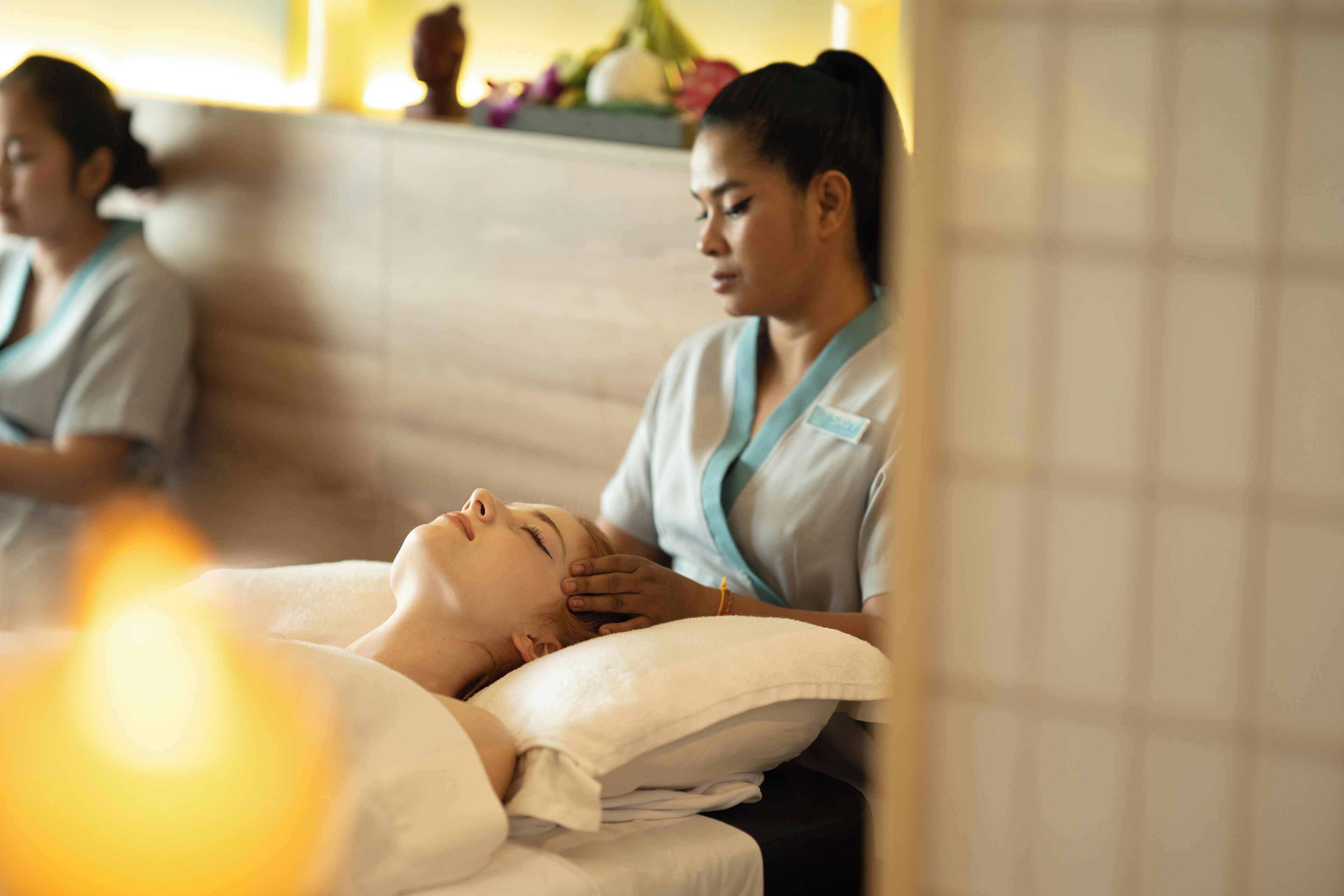 Een wellness omgeving, met een persoon die een massage ontvangt, een massagetherapeut en een zichtbare betegelde muur.