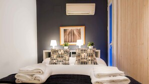 A neatly made bed with folded towels, two bedside lamps, a framed picture on the wall, and an air conditioning unit above. - Welcomer Apartments Valencia (Valencia)