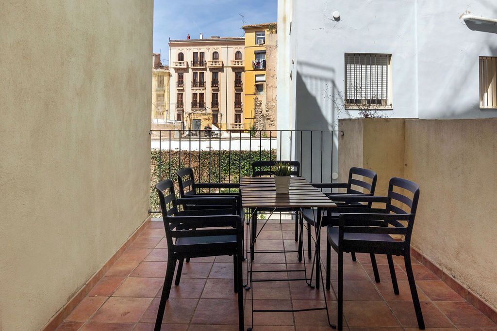 A balcony with a table and chairs, a potted plant, and a view of buildings in the background.