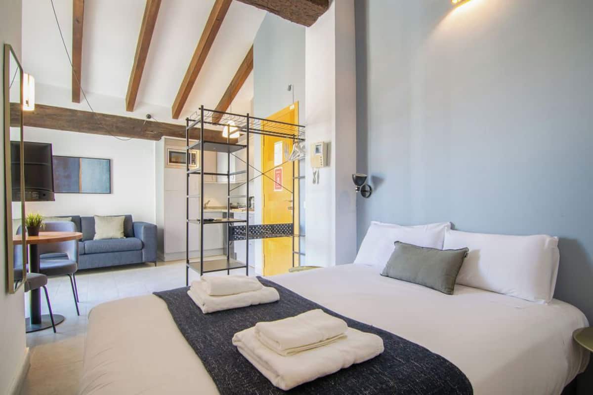 A modern hotel room with a large bed, a desk, a sofa, and a staircase with a metal railing.