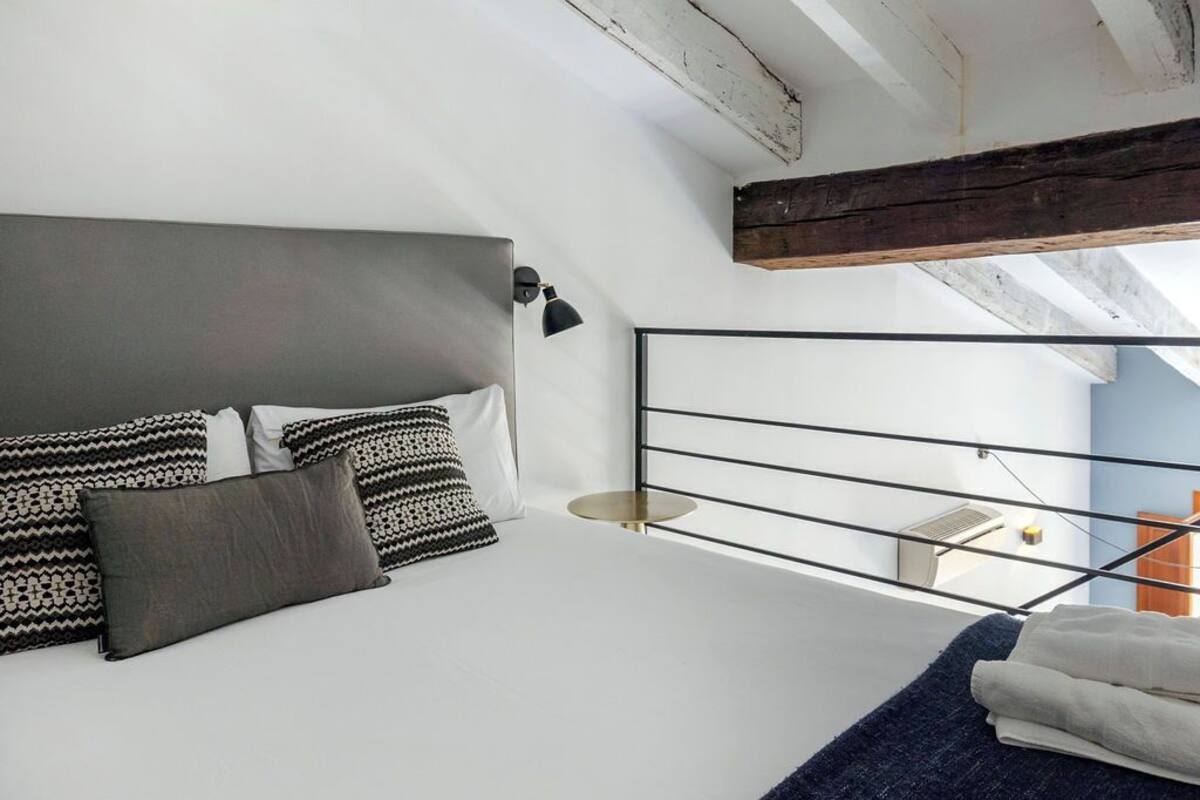A modern bedroom with a large bed, a headboard, and a skylight.
