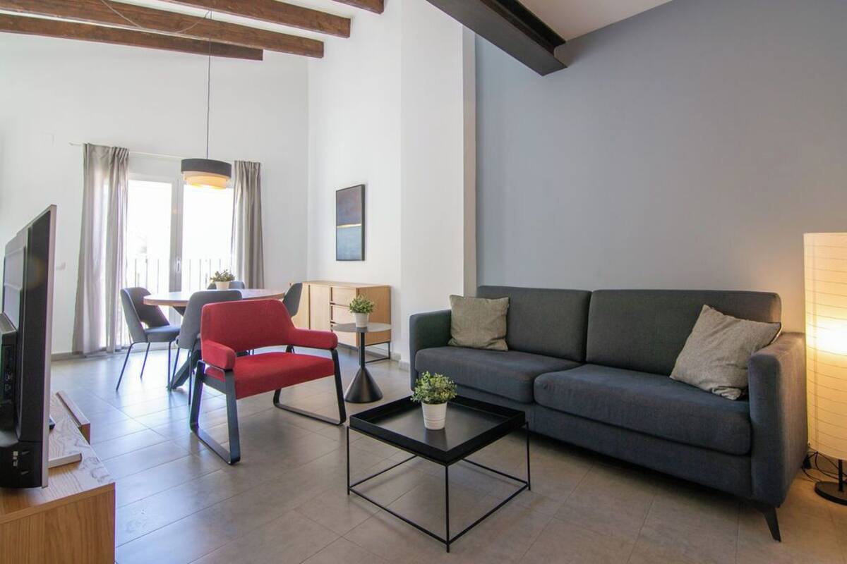 A modern living room with a grey sofa, a red chair, a black coffee table, and a television on a wooden stand.