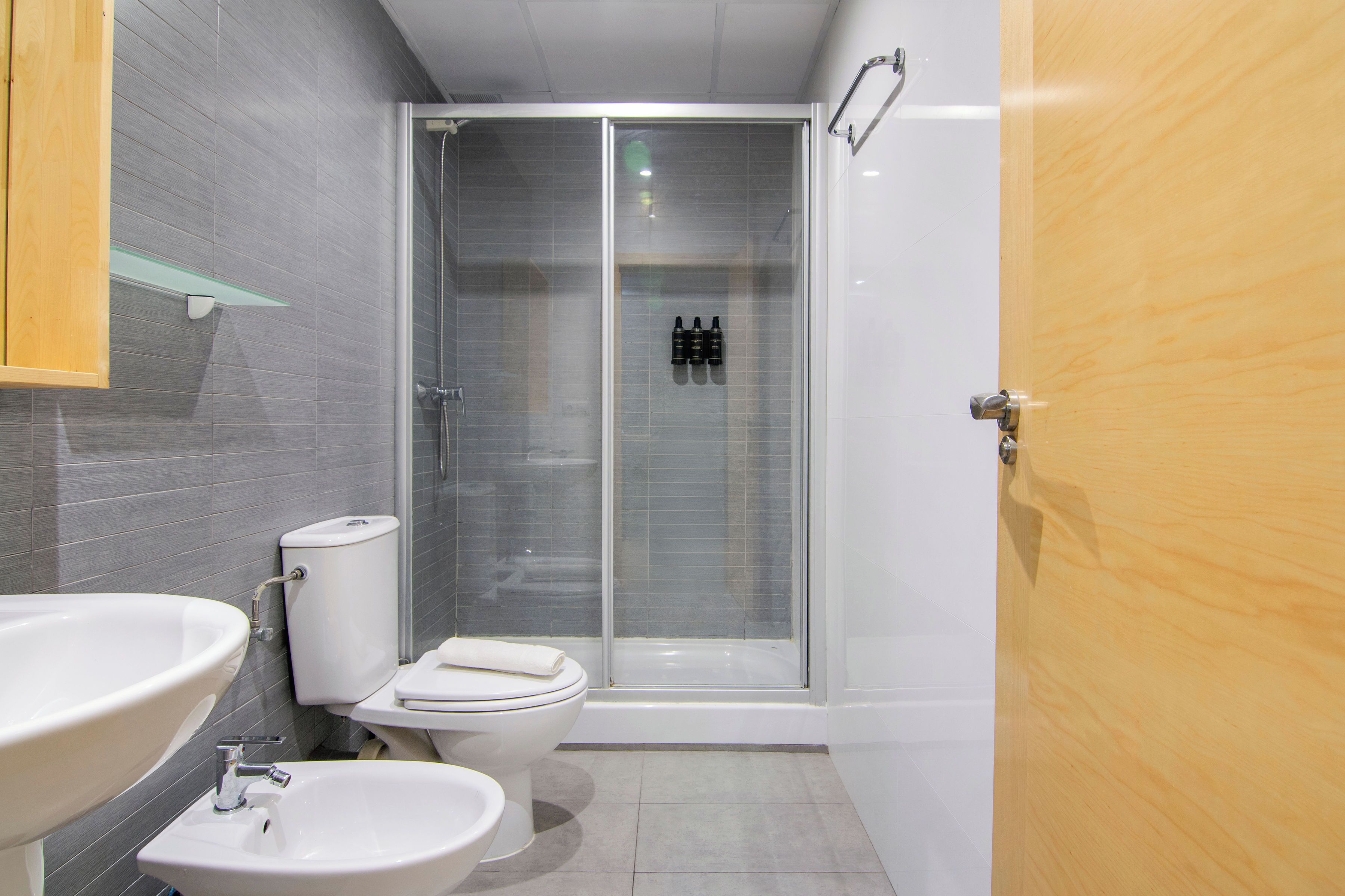 A bathroom with a shower, toilet, sink, and a wooden door.