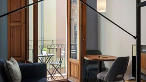 A modern living room with a sofa, a small table, and a chair. There is a balcony with a table and chairs outside. - Welcomer Apartments Valencia (Valencia)