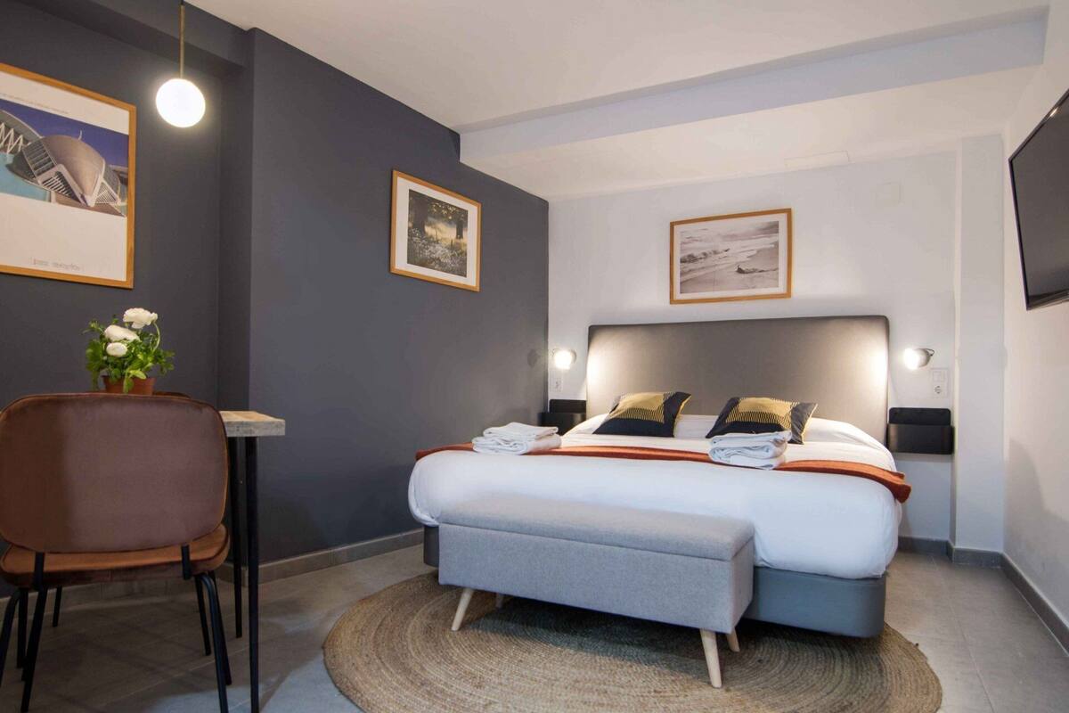 A modern hotel room with a bed, bedside tables, a desk, and a chair.