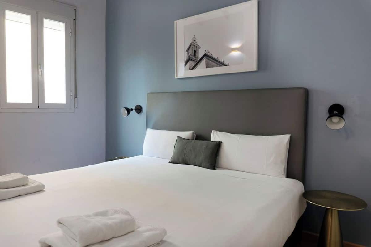 A neatly made bed with white linens, a grey headboard, and a framed picture above it.