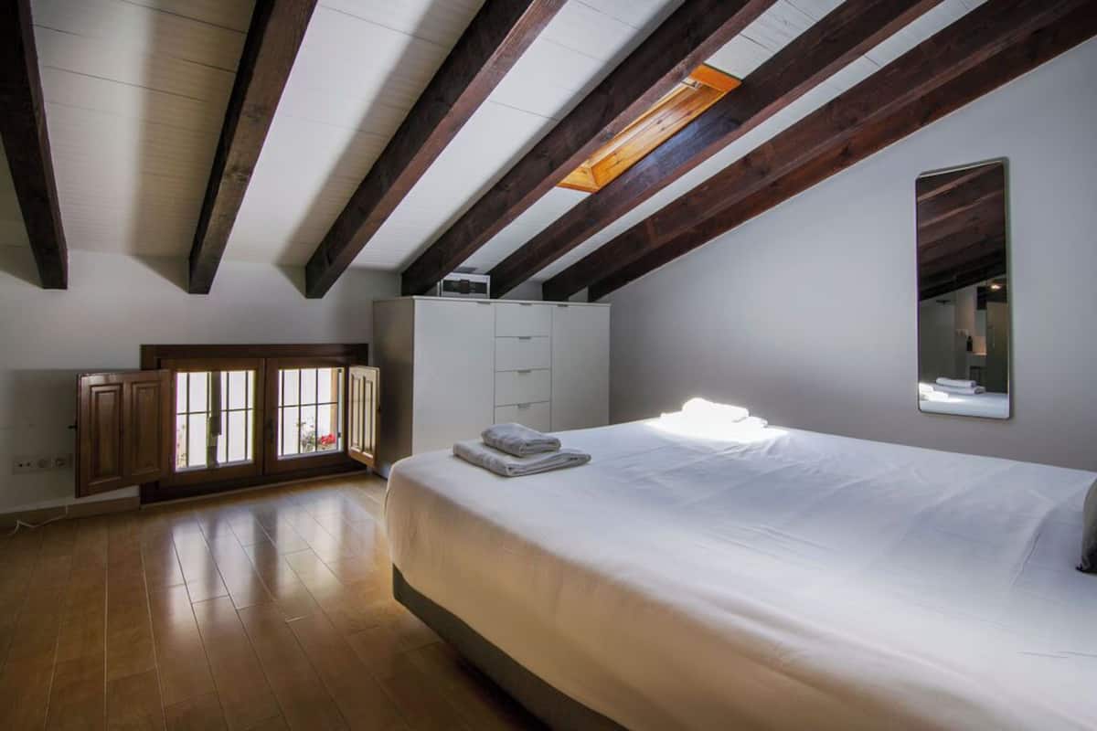 A bedroom with a large bed, wooden beams on the ceiling, a wardrobe, and a window with a view.