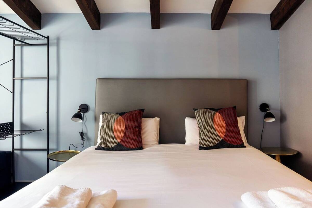 A modern hotel room with a large bed, two bedside lamps, a small round table, and a metal rack.