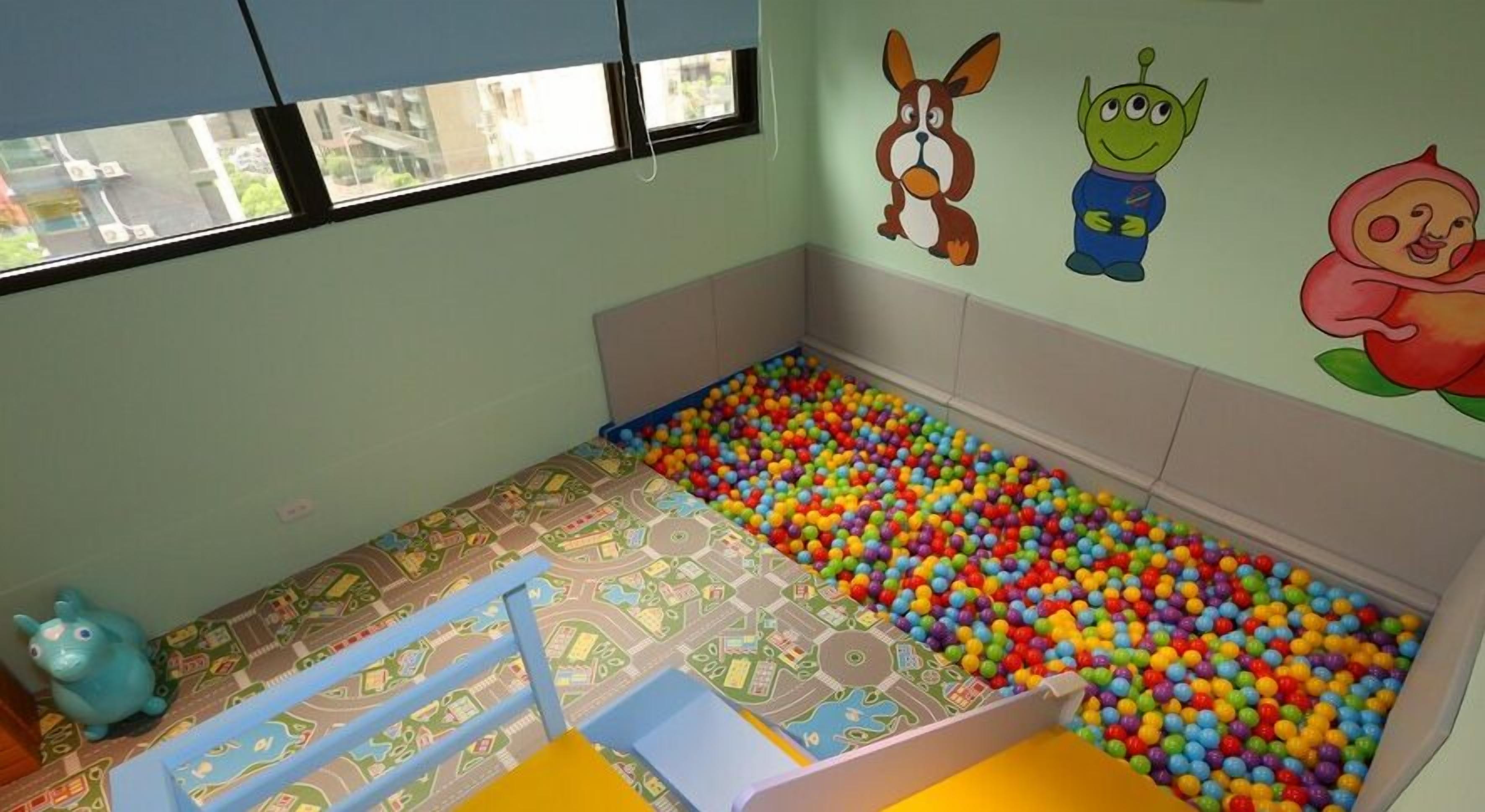 Un cuarto infantil con piscina de pelotas, un coche de juguete y decoraciones de dibujos animados en las paredes.