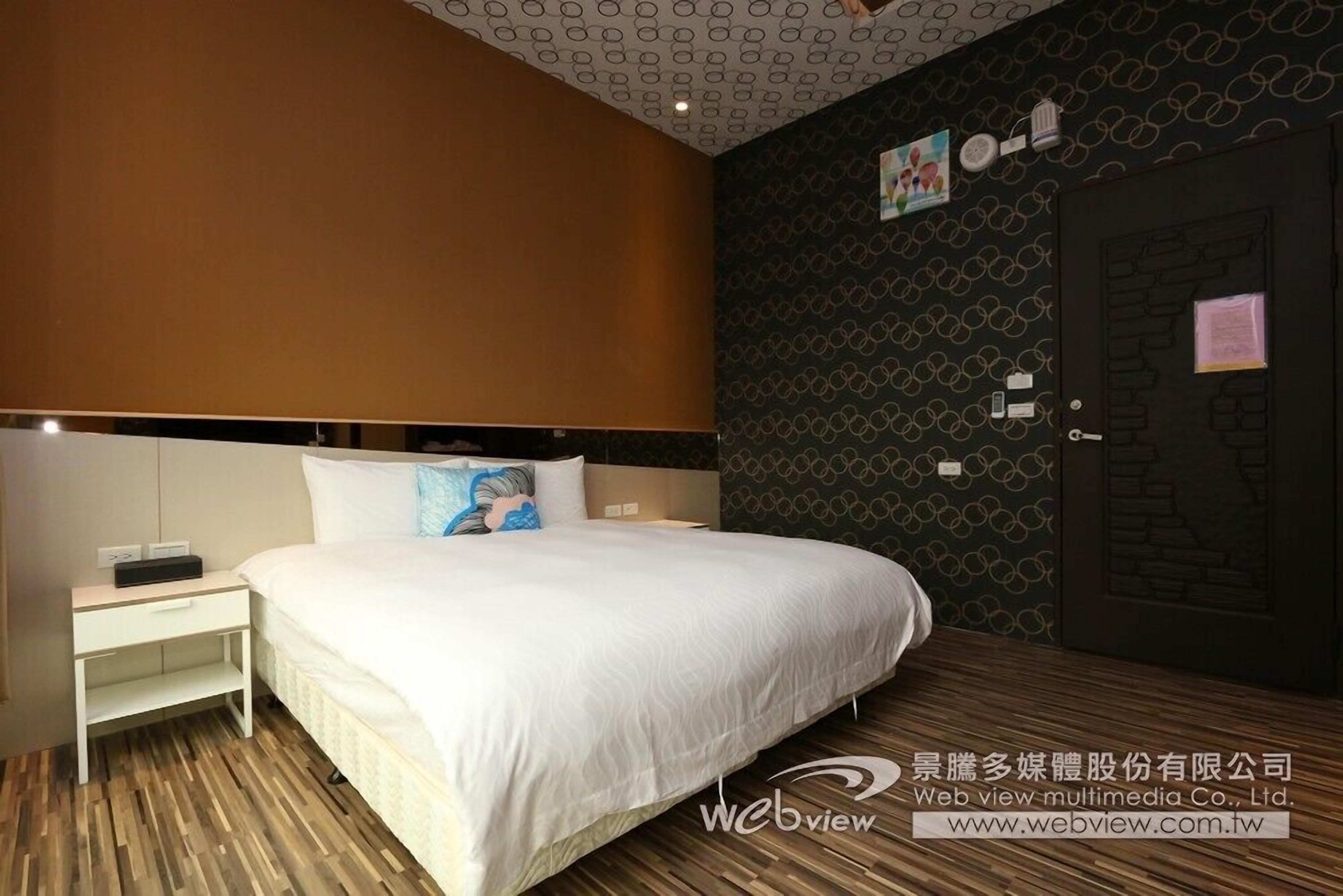 A hotel room with a large bed, a nightstand, a wall clock, and a door with a lock.