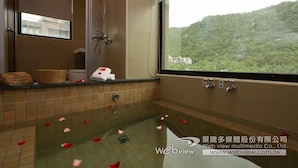 A bathroom with a bathtub filled with rose petals, a shower, and a window offering a view of a green hillside. - Ruo Shui Hotspring Hotel (Jiaoxi)