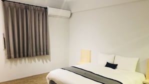 A hotel room with a bed, curtains, an air conditioning unit, a bedside table with a lamp, and a wooden floor. - Ho Young Hotspring Hotel (Jiaoxi)
