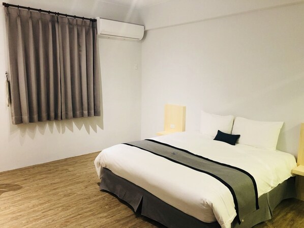 A hotel room with a bed, curtains, an air conditioning unit, a bedside table with a lamp, and a wooden floor. - Ho Young Hotspring Hotel (Jiaoxi)