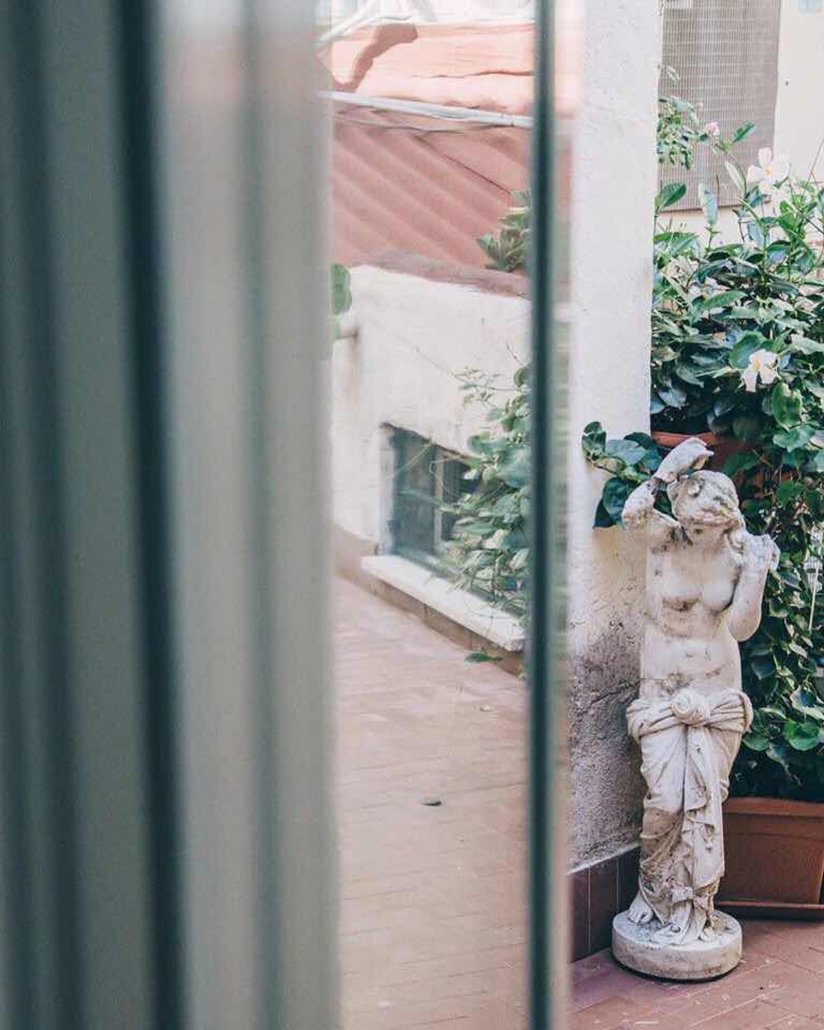 A statue of a woman holding a branch, positioned next to a wall with a potted plant.