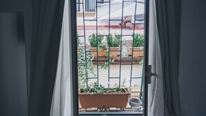 A view through a window with a metal grid, potted plants, and a balcony railing. - Spagna Rooms (Rome)