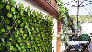 A patio area with a metal trellis covered in green foliage, a wooden table, and a folding chair. - Spagna Rooms (Rome)