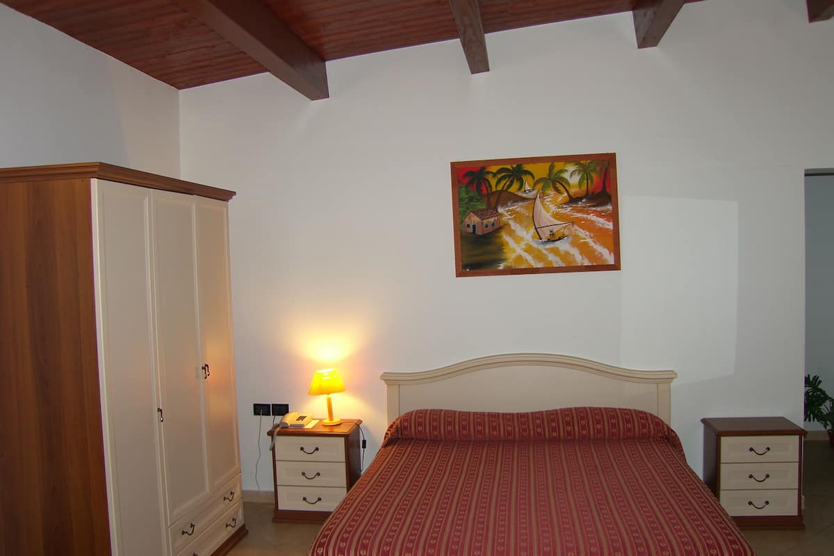 A bedroom with a bed, a wardrobe, a nightstand with a lamp, and a painting on the wall.