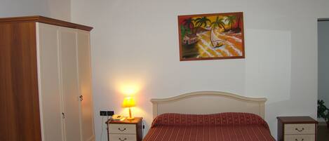A bedroom with a bed, a wardrobe, a nightstand with a lamp, and a painting on the wall.