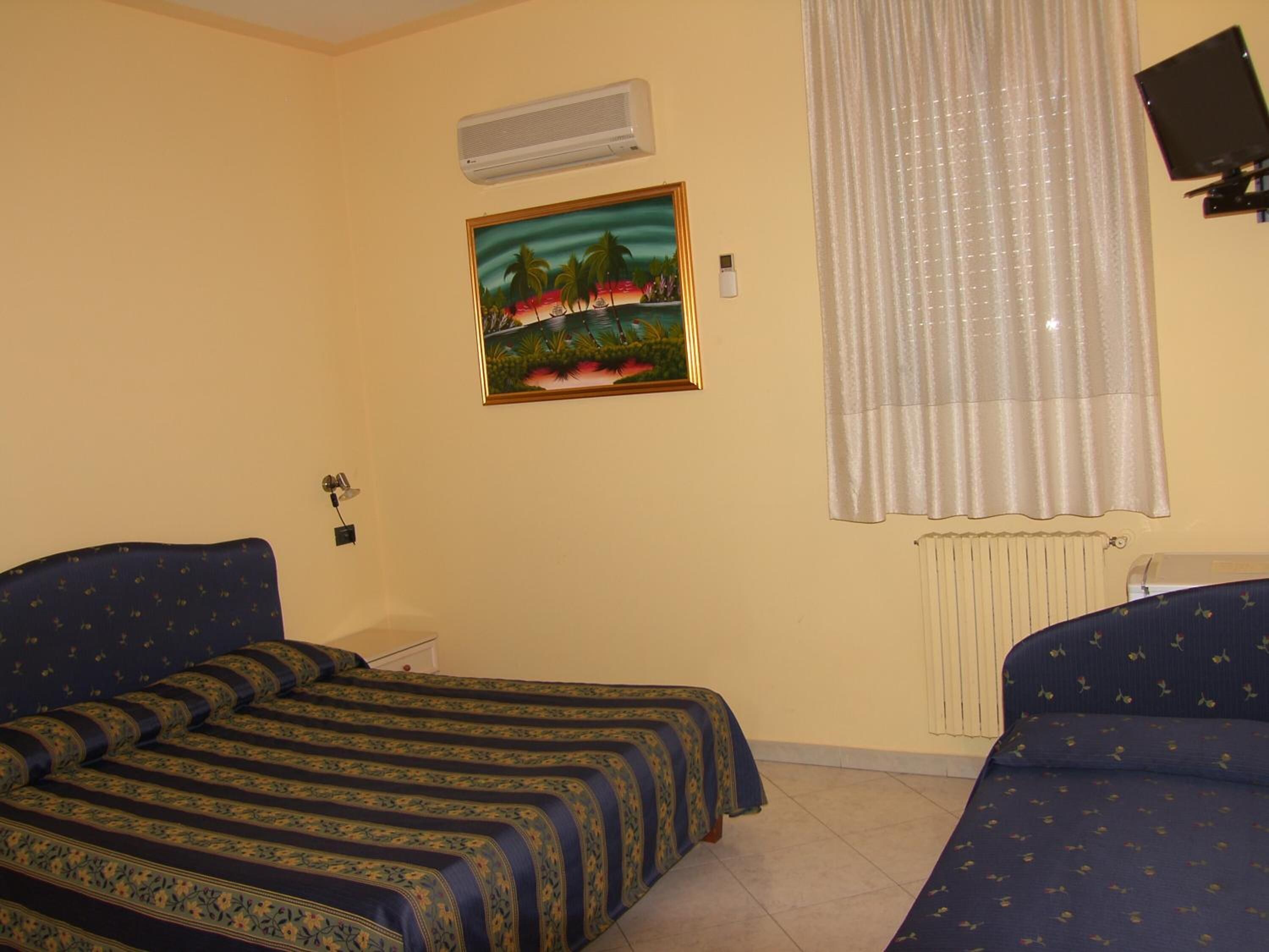 Una habitación con dos camas, un cuadro, aire acondicionado, una ventana con cortinas y un televisor.