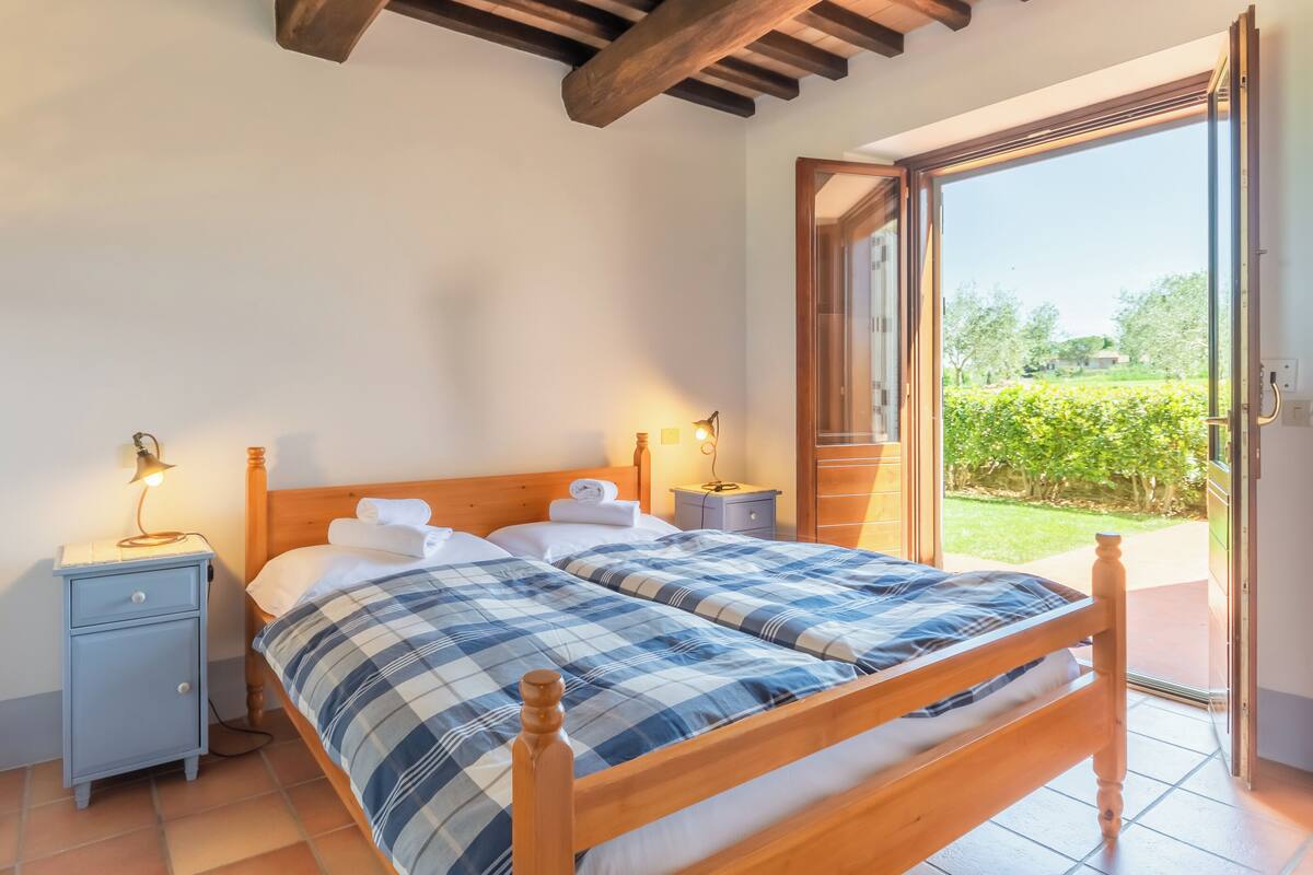 Une chambre à coucher avec un lit en bois, deux tables de chevet, une commode et une porte ouverte donnant sur un jardin.