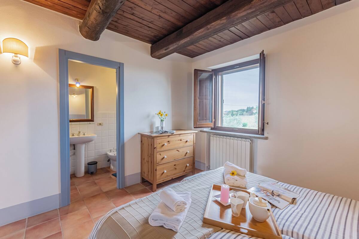 Une chambre avec un plafond en bois, une fenêtre offrant une belle vue, une table de chevet avec des articles de toilette et un lit recouvert d’une couvre-lit à rayures.