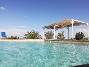 Una piscina cristalina con un pabellón blanco y una silla azul.