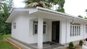 A single-story white building with a covered porch, a small front entrance, and a car parked outside.