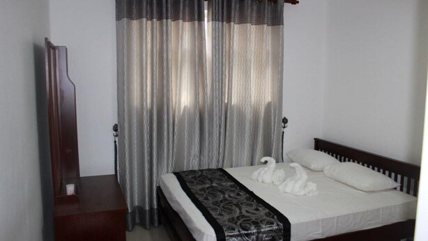 A hotel room with a bed, a wooden nightstand, a mirror, and a curtain.