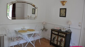 A room with a white table, two chairs, a mirror, a cabinet with paintings, and a radiator.