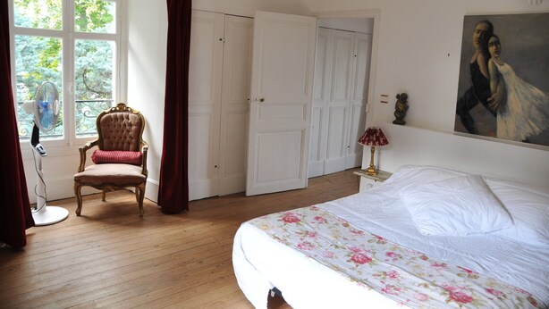 A bedroom with a bed, a chair, a wardrobe, and a painting on the wall.