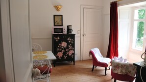 A room with a wooden floor, a white door, a black cabinet with floral patterns, a red chair, and a table with a white tablecloth.