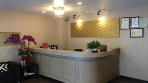 A reception area with a curved reception desk, a chandelier, framed certificates on the wall, and a potted plant. - HUA CHUN LIN Hotel (New Taipei City)